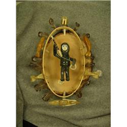 Soapstone hunter with ivory face and harpoon surrounded by elliptical hoop with feathers and soapsto