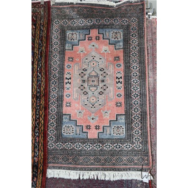 Wool blend throw carpet with center medallion, fringed edge and highlights of soft red, blues, black