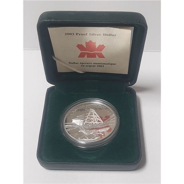 2003 Proof Silver Dollar. Commemorates the 100th Anniversary of a blacksmith throwing a hammer at a 