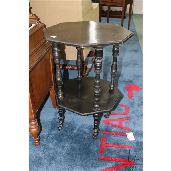 Antique octagonal two tier table with ebonized finish and porcelain castors.  Note: one leg needs re