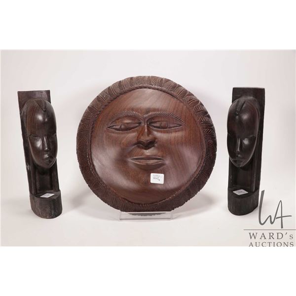 Three hand made wooden African carvings including set of book ends with carved faces and a round sun