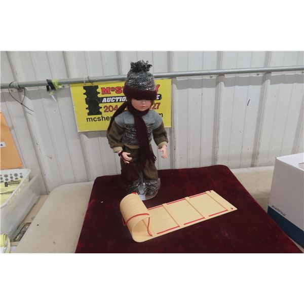 Porcelain Doll With Stand and Plastic Sleigh, Measuring 19 in. Tall.