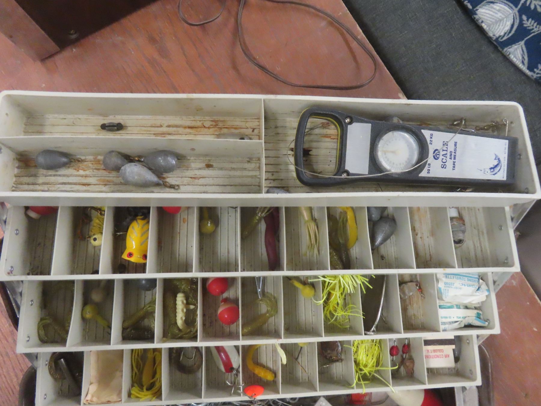 A fishing rod with a reel attached, a tackle box filled with hooks, lures, and sinkers, and a fishing net lying nearby