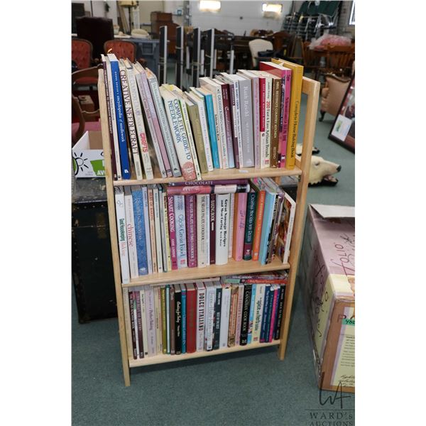 Folding three tier blonde wooden bookcase with a large selection of cookery books and some needlecra