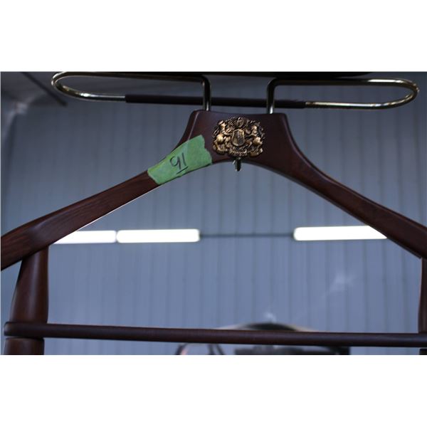 Wooden valet stand featuring a dark wood finish, equipped with a brass crest detailing two lions and