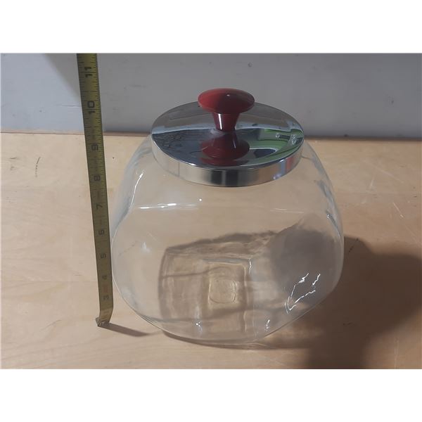 Vintage tilted glass penny candy jar with a chrome lid and a red knob.