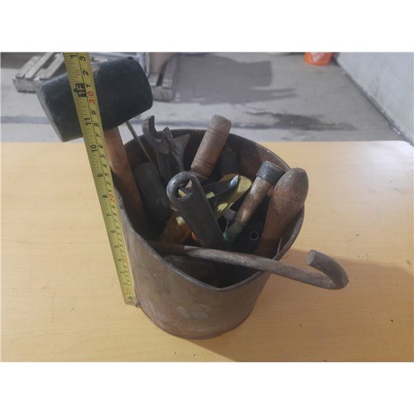 Vintage industrial metal bucket filled with assorted old hand tools.