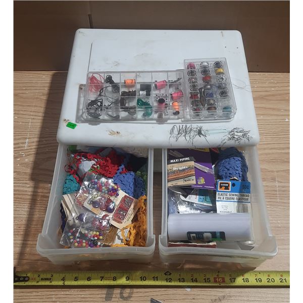 This is a clear plastic craft supply organizer box filled with assorted sewing notions, threads, and