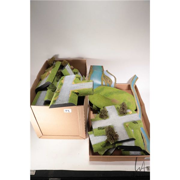 Two boxes containing a large selection of tabletop terrain including roads, rivers, grass mounts etc