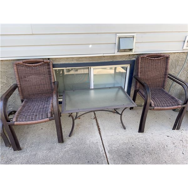 Outdoor patio set including a rectangular glass-top metal table and 4 brown wicker armchairs. Table