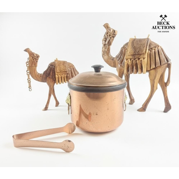 Two Carved Wooden Camel Figurines, A Copper Ice Bucket With A Lid, And Matching Copper Tongs. 