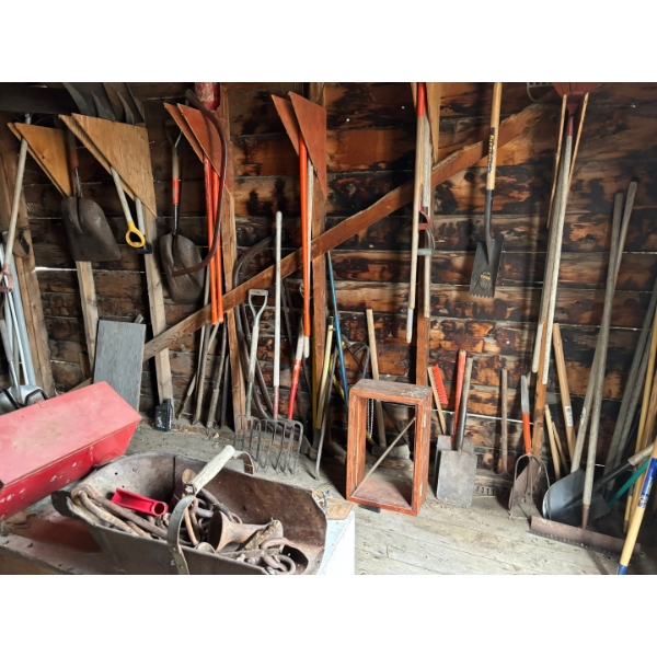 All Yard items on the wall, including pitchforks shovels brooms all sorts of shovels chains 