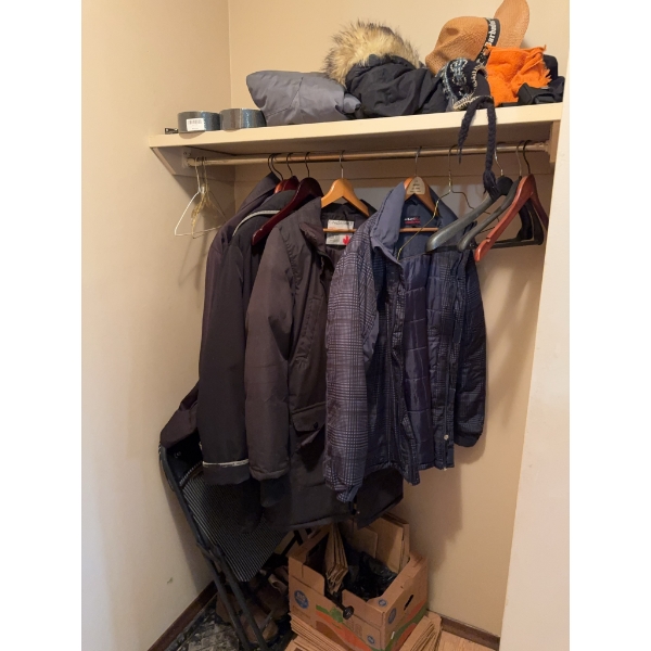 Multiple adult-sized jackets and outerwear on wooden and plastic hangers, along with hats, a sleepin