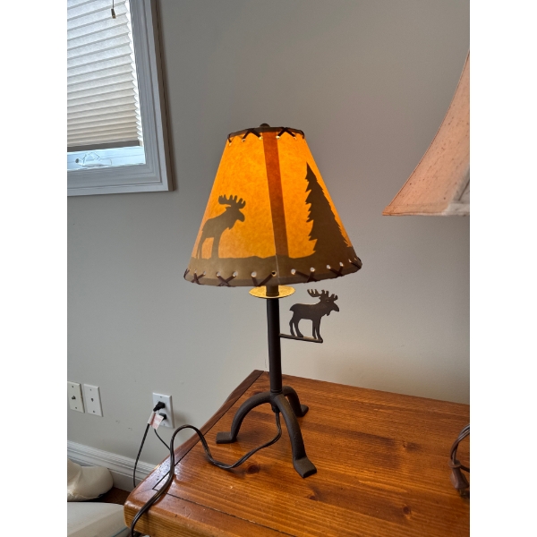 This is a rustic moose themed table lamp featuring a metal base and a faux leather or rawhide shade