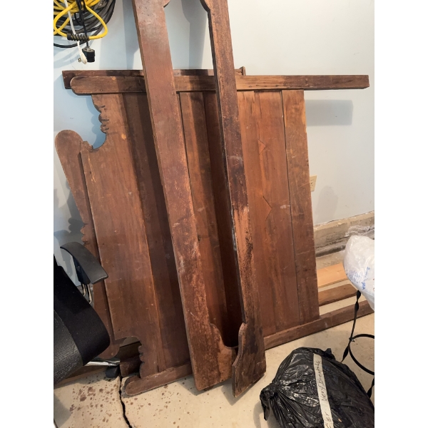 Disassembled wooden bed frame including headboard, footboard, and side rails. The frame shows wear a