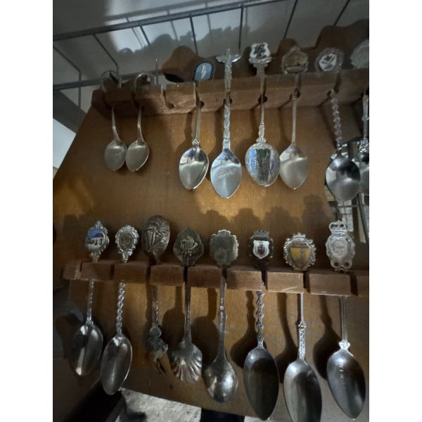 collection of souvenir or collectible spoons on a custom wooden display rack shaped like the contine