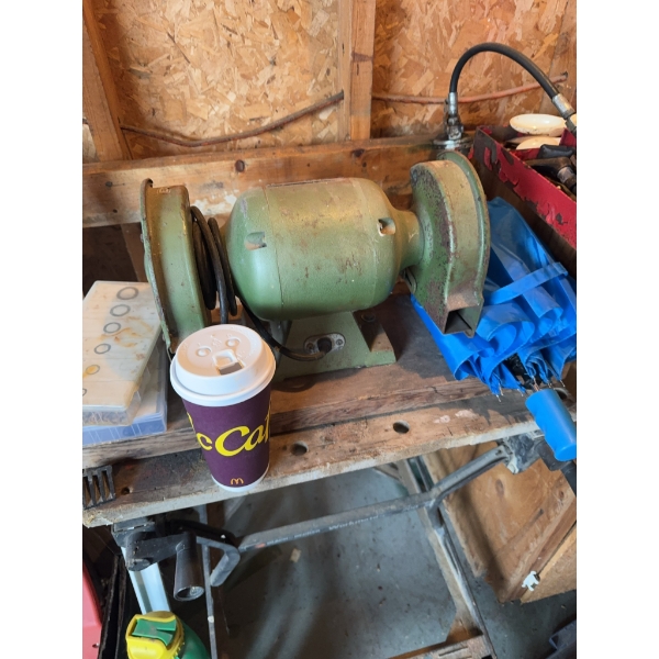 Double wheel bench grinder with a green metal body, mounted on a wooden workbench. This tool is used