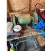 Image 1 : Double wheel bench grinder with a green metal body, mounted on a wooden workbench. This tool is used