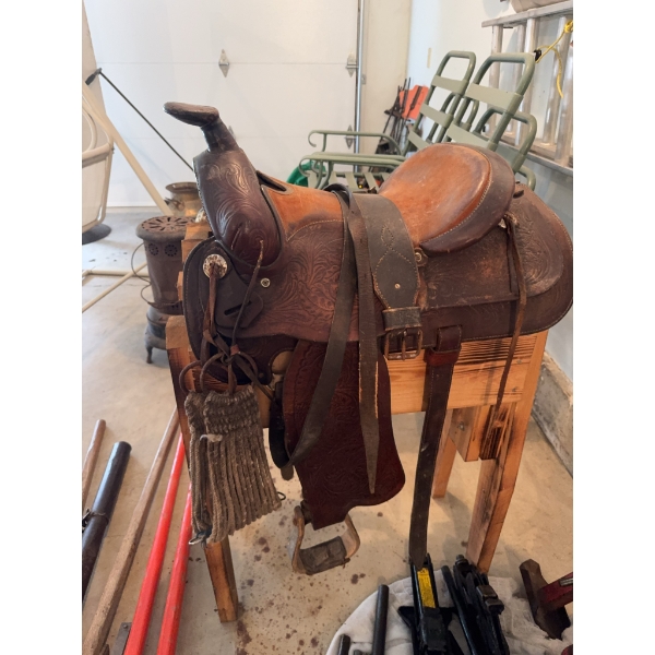 Tooled leather Western horse saddle featuring floral designs, metal conchos, and attached stirrups. 