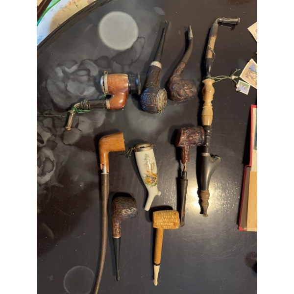 Nine tobacco pipes featuring various materials including wood, porcelain, and corn cob. Includes car