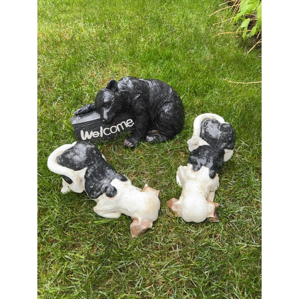 Three animal garden statues: one black bear holding a 'Welcome' sign and two black and white dog fig