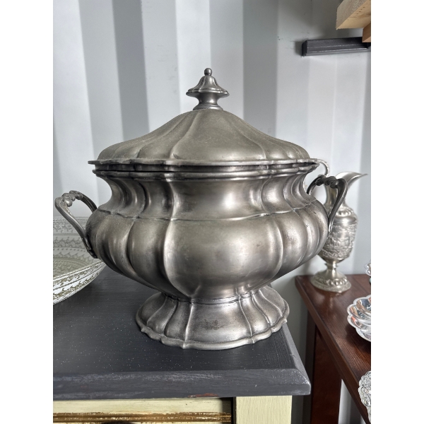  antique pewter soup tureen with a lid, featuring a molded, multi-lobed design and two handles. 
Mat