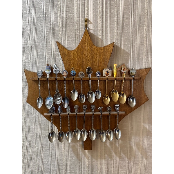 collection of Canadian souvenir spoons displayed on a maple leaf-shaped wooden rack. 
Souvenir spoon