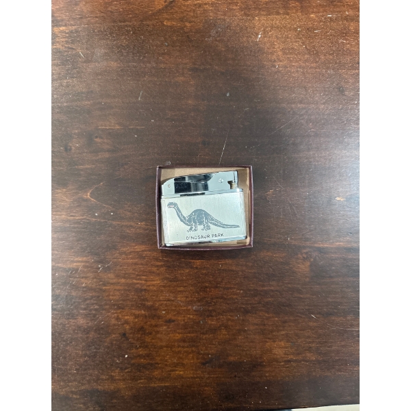 vintage lighter featuring a dinosaur design and the text "DINOSAUR PARK".