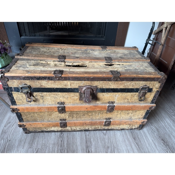 Wood and metal steamer trunk with exterior metal hardware and wooden slats. The exterior surface sho