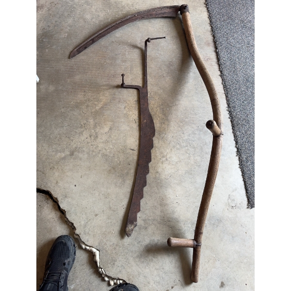 Traditional scythe with a wooden handle and metal blade, along with a metal adjustable hay rake atta